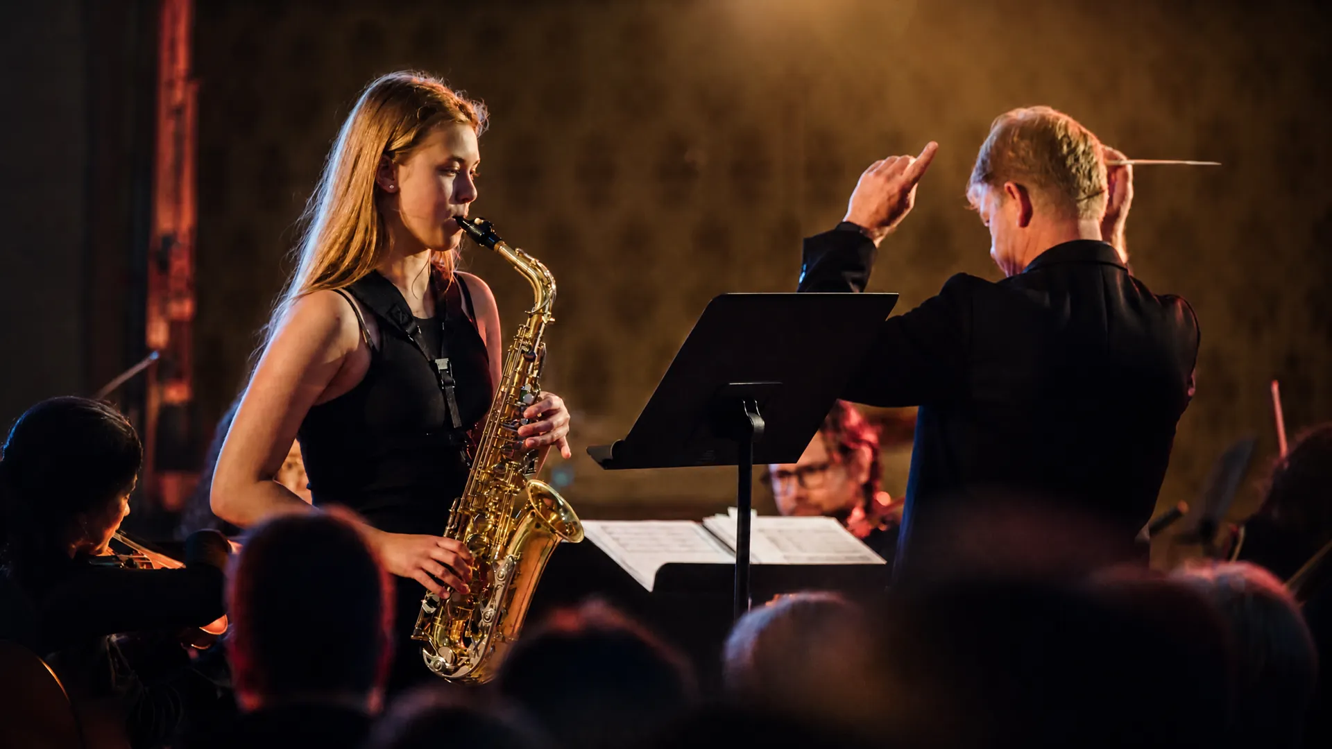 Žákyně hraje na saxofon za doprovodu orchestru při večerním koncertě.